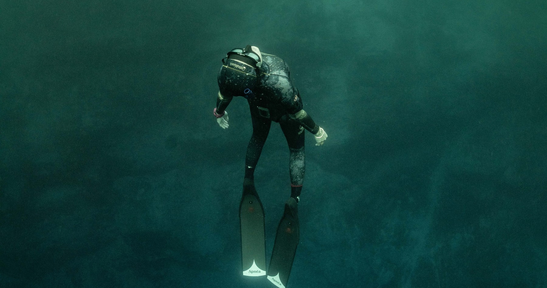 A freediver descending through murky green water