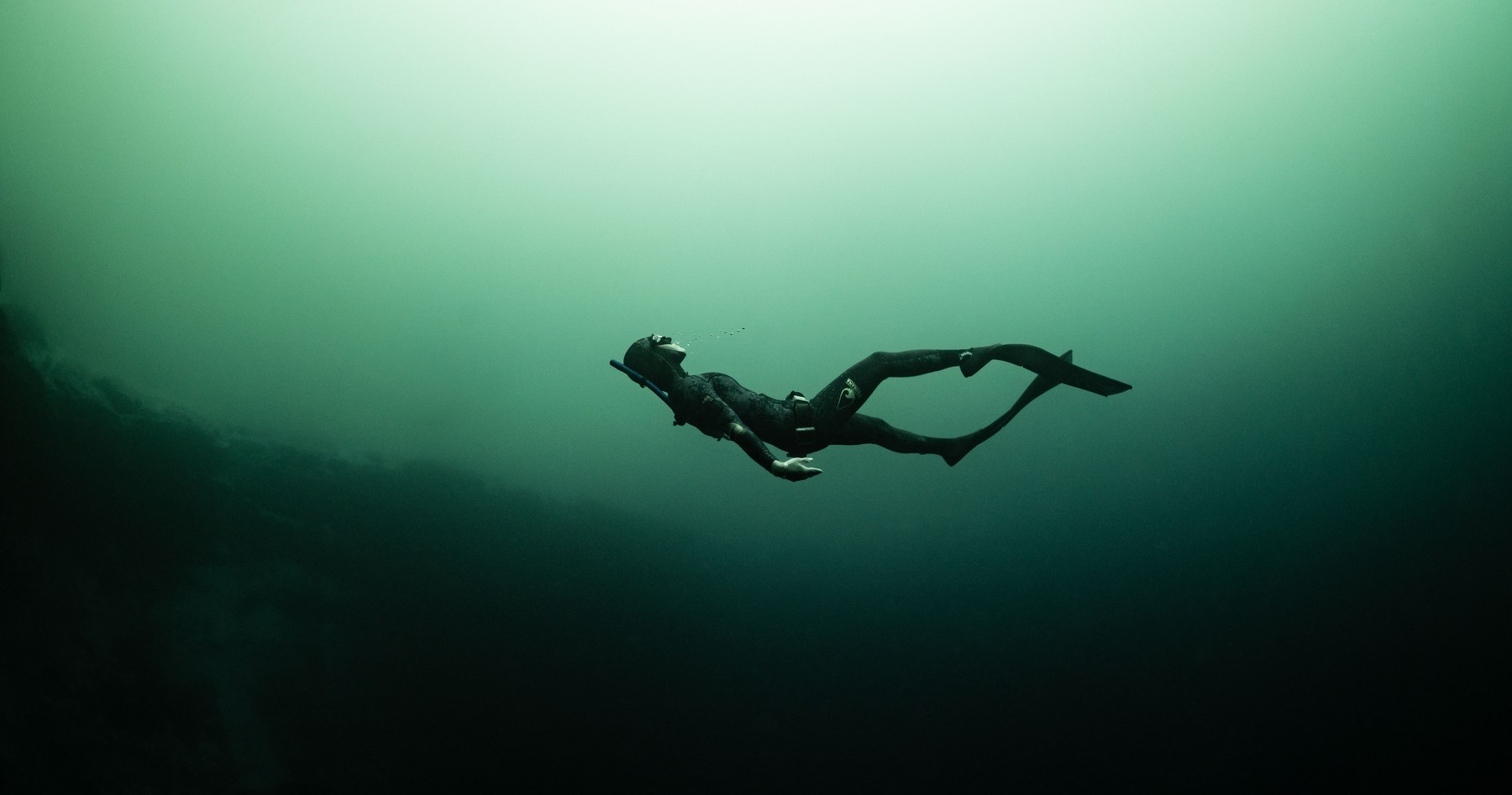 A freediver descending into a cenote, light streaming from the surface